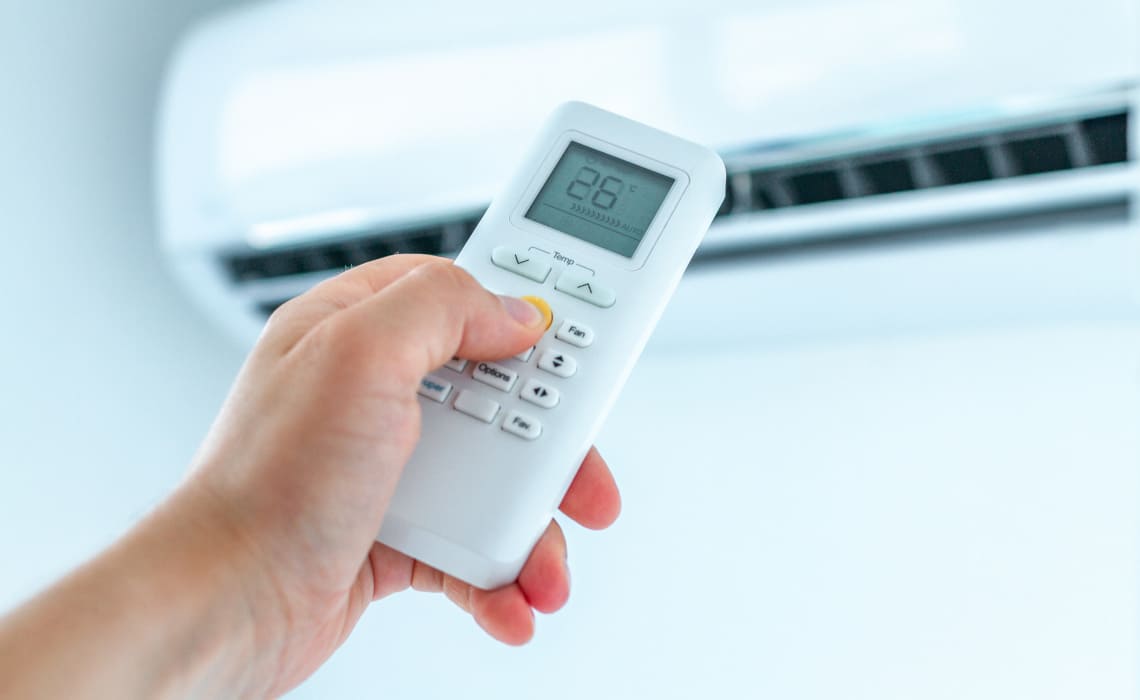 Klimaanlage einbauen lassen - Hand hält eine Fernbedienung und stellt die Temperatur einer modernen Klimaanlage ein