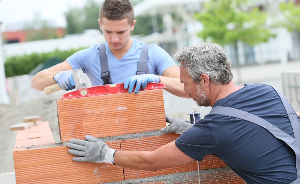 Maurerarbeiten - Maurer setzen Ziegelsteine beim Bau einer tragenden Mauer auf der Baustelle